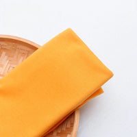 Un morceau de Tissu en jersey simple au mètre de Longan Craft France, en polyester-coton multicolore, est soigneusement plié sur un plateau rond en bambou sur fond blanc.