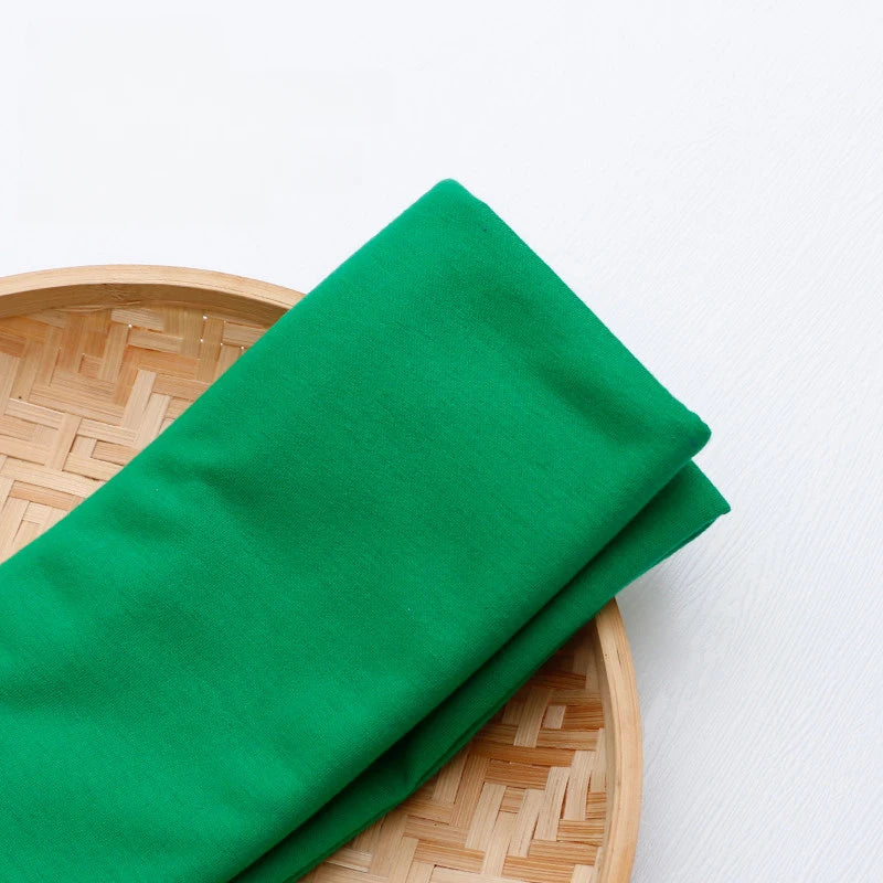 Un morceau de Tissu en jersey simple au mètre de Longan Craft France, en polyester-coton multicolore, est plié sur un plateau rond en bambou sur fond blanc. Idéal pour la confection de vêtements décontractés.