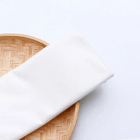 Un morceau plié de Tissu en jersey simple au mètre de Longan Craft France repose sur un plateau rond tissé de couleur claire, sur fond blanc - un jersey polyester-coton parfait pour les vêtements décontractés.