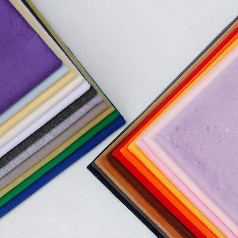 Deux piles bien rangées de "Tissu en jersey simple au mètre" de Longan Craft France en polyester-coton, idéal pour les t-shirts et les vêtements décontractés, sont présentées en violet, jaune, gris, vert, orange et marron sur un fond clair.