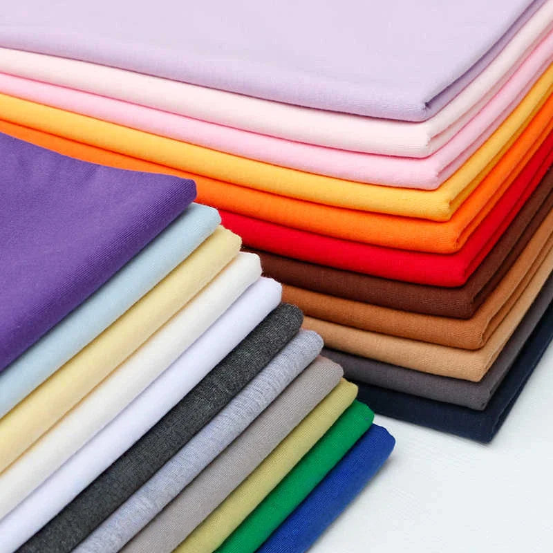 A stack of Longan Craft France Tissu en jersey simple au mètre, un jersey polyester-coton multicolore, idéal pour t-shirts ou vêtements décontractés, est soigneusement disposée sur une surface blanche.