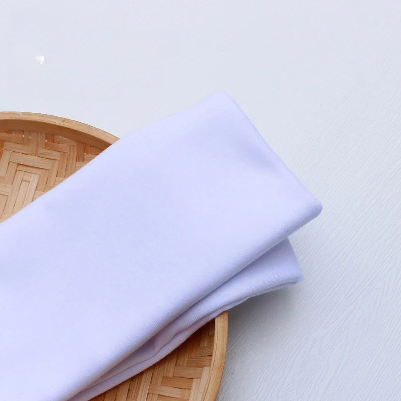 Un morceau de Tissu en jersey simple au mètre de Longan Craft France, idéal pour vêtements décontractés, repose sur un plateau en bambou tressé rond, posé sur une surface claire.