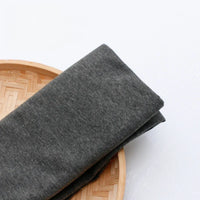 Un morceau de Tissu en jersey simple au mètre de Longan Craft France, fabriqué en polyester-coton multicolore pour une tenue décontractée, est soigneusement présenté sur un plateau rond en bambou tressé sur fond blanc.