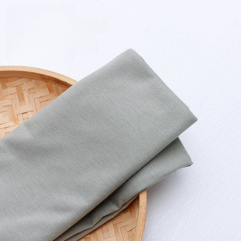 Un morceau de jersey multicolore en polyester et coton de Longan Craft France est soigneusement plié sur un plateau rond en bambou, prêt à être utilisé pour créer une tenue décontractée.