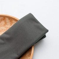 Un morceau de jersey multicolore en polyester-coton de Longan Craft France repose sur le bord d'un plateau en bambou tressé, posé sur une surface blanche.