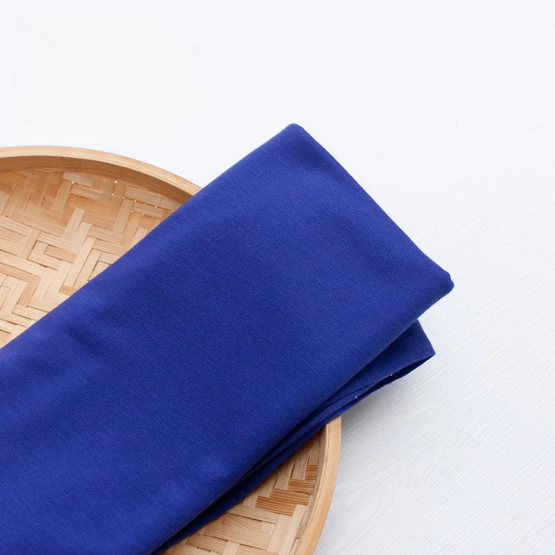 Un morceau plié de Tissu en jersey simple au mètre de Longan Craft France en bleu royal repose sur un plateau rond en bambou, posé sur une surface blanche.