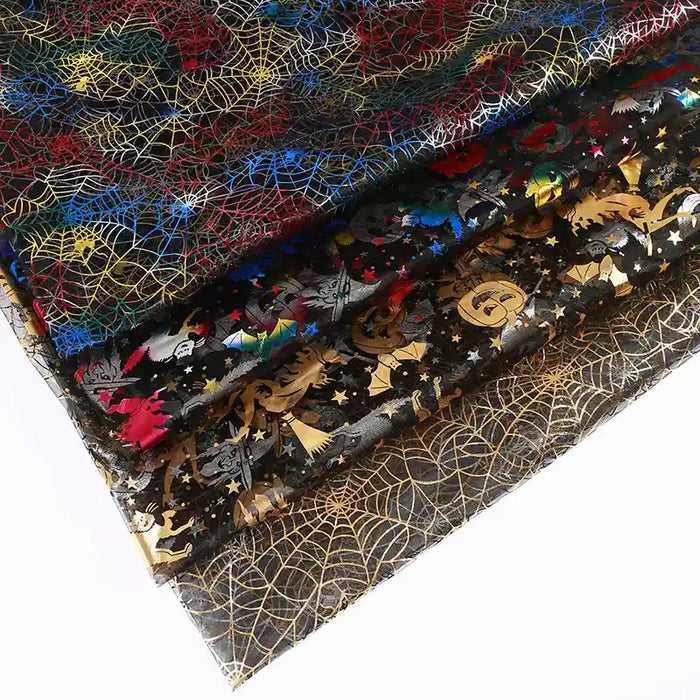Quatre feuilles de tissu organza toile d'araignée au mètre de Longan Craft France, transparentes et colorées avec des motifs métalliques d'Halloween, sont empilées sur du blanc - idéal pour les déguisements ou les travaux manuels.