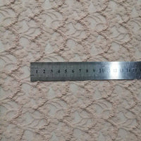 Une règle argentée mesurant les centimètres est posée sur la Dentelle extensible au mètre de Longan Craft France, une dentelle extensible beige clair brodée de franges florales, mettant en valeur la texture et le design détaillés du tissu.
