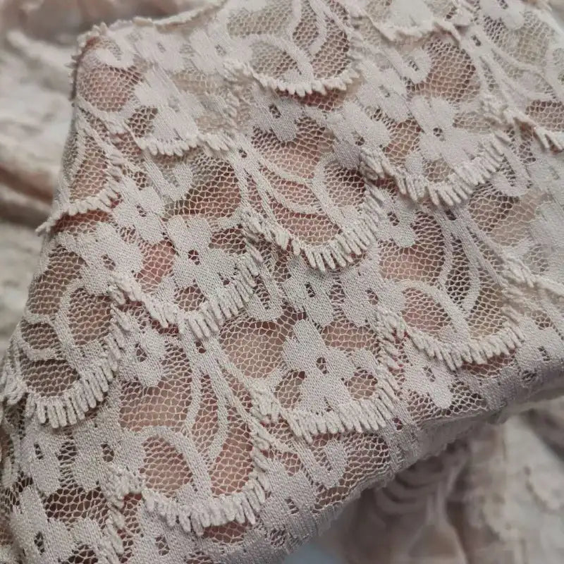 Gros plan d'une main tenant la "Dentelle extensible au mètre" de Longan Craft France, un délicat tissu de dentelle florale aux coutures complexes, parfait pour les robes et la lingerie de bricolage.