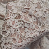 Gros plan d'une main tenant la "Dentelle extensible au mètre" de Longan Craft France, un délicat tissu de dentelle florale aux coutures complexes, parfait pour les robes et la lingerie de bricolage.