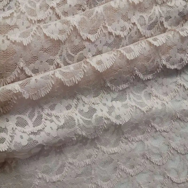 Un gros plan de la dentelle extensible au mètre de Longan Craft France révèle la broderie florale frangée complexe et les textures délicates - un tissu de dentelle DIY idéal pour les peignoirs et la lingerie.