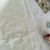 Gros plan sur le Linon de coton imprimé à petits pois au mètre par Longan Craft France, un tissu respirant bleu clair 100 % coton aux bords effilochés, présenté à côté de dentelle, de fleurs séchées, de citrons en tranches et d'une pince à coudre bleue.
