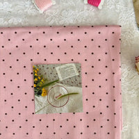 Un morceau de Linon de coton imprimé à petits pois au mètre par Longan Craft France est posé à plat, avec une carte florale et un cercle à broder sur le dessus. Des bobines de fil rose et du tissu à dentelle se trouvent à proximité. Ce tissu linon 100 % coton est léger et respirant.