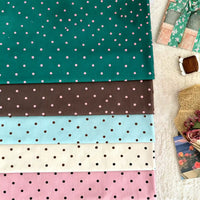 Cinq pièces pliées de Longan Craft France Linon de coton imprimé à petits pois en sarcelle, marron, bleu clair, crème et rose sont empilées, avec un cadeau, une bobine de fil marron, un panier et une carte florale à proximité. 100% coton - parfait pour une tenue décontractée.