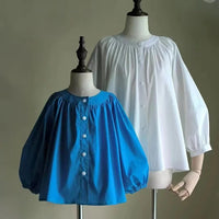 Deux mannequins portent le patron de couture PDF "Blouse à encolure ronde smockée avec manches raglan" de Longan Craft France : l'une est bleu vif, l'autre blanche. Toutes deux ont une coupe ample, une encolure ronde froncée et un devant boutonné sur un fond uni.