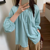 Une personne porte la Blouse à encolure ronde smockée avec manches raglan (patron PDF gratuit) de Longan Craft France, l'associe à un pantalon beige et prend un selfie miroir à l'intérieur en tenant un téléphone et un sac à motifs marron.