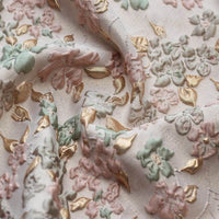 Un gros plan du tissu brocart floral à bulles douces au mètre de Longan Craft France montre des fleurs gaufrées rose pastel, vertes et dorées sur un fond clair - idéal pour les vêtements ou l'ameublement avec des détails texturés uniques.