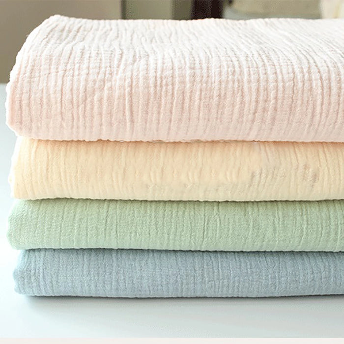 Quatre couvertures en gaze pastel - rose, crème, vert et bleu clair - sont pliées sur une surface blanche. Réalisées en tissu double gaze doux au mètre de Longan Craft France, elles offrent une douceur exceptionnelle, idéale pour les vêtements de bébé.