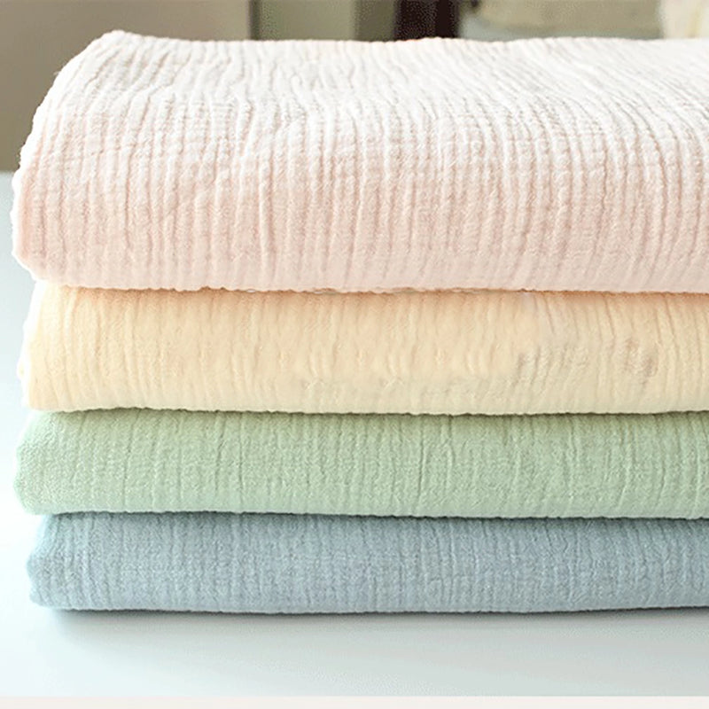 Quatre couvertures en gaze pastel - rose, crème, vert et bleu clair - sont pliées sur une surface blanche. Réalisées en tissu double gaze doux au mètre de Longan Craft France, elles offrent une douceur exceptionnelle, idéale pour les vêtements de bébé.