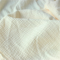 Gros plan sur le Tissu double gaze doux au mètre de Longan Craft France, de couleur crème avec un quadrillage subtil. Doux, léger et idéal pour les vêtements de bébé, ce tissu présente une texture visible et des plis doux.