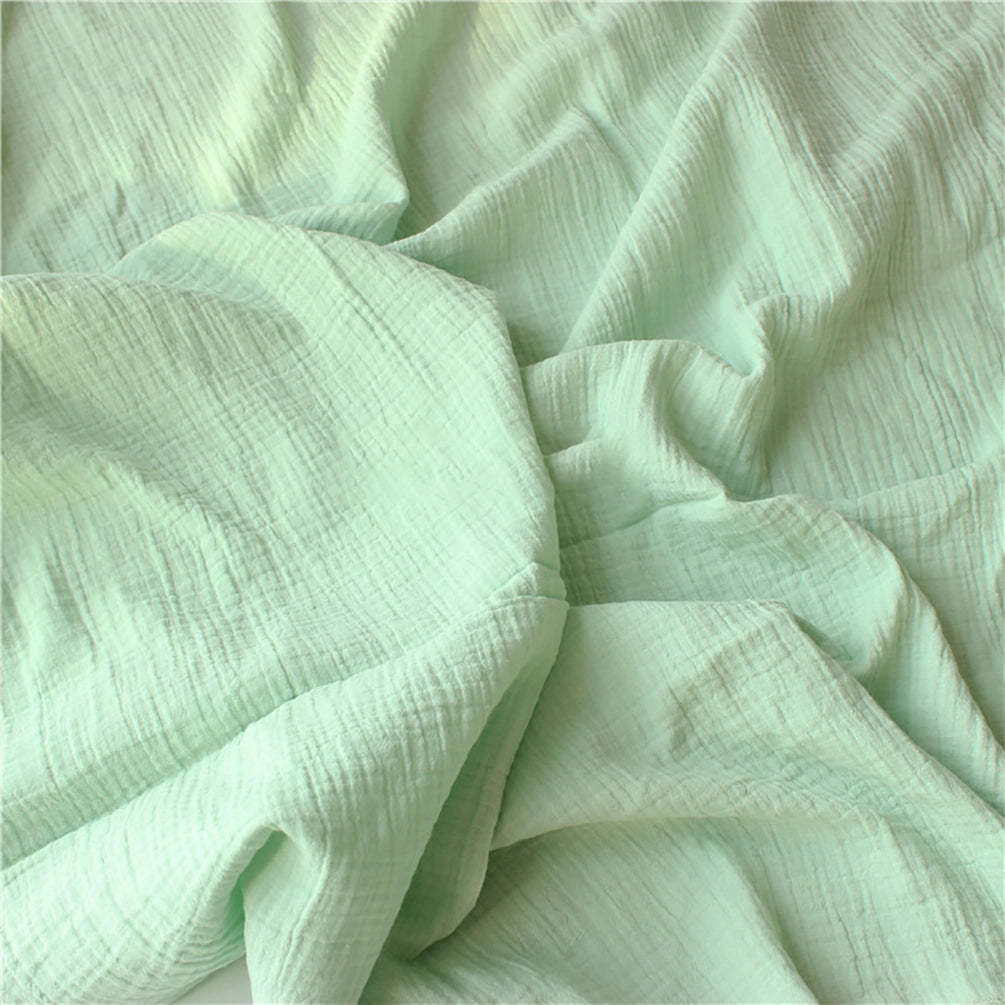 Le Tissu double gaze doux au mètre de Longan Craft France est un tissu vert clair avec des plis visibles et des plis souples, créant une surface douce et texturée, idéale pour les vêtements de bébé grâce à sa douceur exceptionnelle.