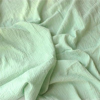Le Tissu double gaze doux au mètre de Longan Craft France est un tissu vert clair avec des plis visibles et des plis souples, créant une surface douce et texturée, idéale pour les vêtements de bébé grâce à sa douceur exceptionnelle.