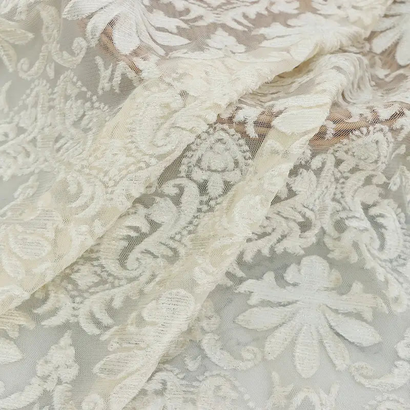 Un gros plan du tissu dentelle burnout au mètre, blanc, de Longan Craft France, montre ses motifs floraux et feuillus complexes, sa texture délicate en polyester semi-transparent et son drapé doux, idéal pour les peignoirs et les hauts féminins.