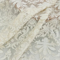 Un gros plan du tissu dentelle burnout au mètre, blanc, de Longan Craft France, montre ses motifs floraux et feuillus complexes, sa texture délicate en polyester semi-transparent et son drapé doux, idéal pour les peignoirs et les hauts féminins.
