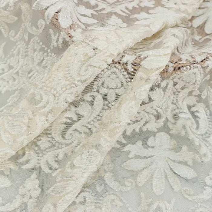 Un gros plan du tissu dentelle burnout au mètre, blanc, de Longan Craft France, montre ses motifs floraux et feuillus complexes, sa texture délicate en polyester semi-transparent et son drapé doux, idéal pour les peignoirs et les hauts féminins.