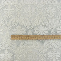 Une règle en bois de 30 cm est posée sur le "Tissu dentelle burnout au mètre" blanc de Longan Craft France, qui présente un motif floral damassé idéal pour les robes et les hauts féminins.