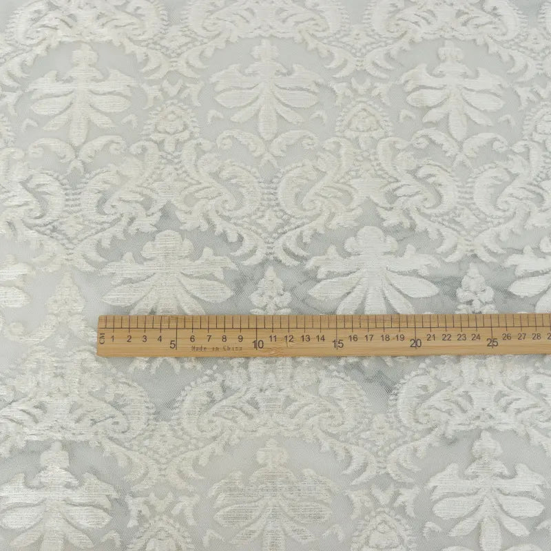 Une règle en bois de 30 cm est posée sur le "Tissu dentelle burnout au mètre" blanc de Longan Craft France, qui présente un motif floral damassé idéal pour les robes et les hauts féminins.