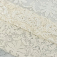 Un gros plan de deux pièces superposées de Tissu dentelle burnout au mètre de Longan Craft France montre des motifs floraux et de feuilles complexes blanc cassé et beige, avec un motif de dentelle assorti à l'arrière-plan. Idéal pour les peignoirs et les hauts féminins.