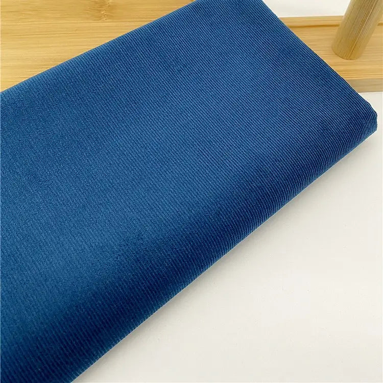 Gros plan sur Tissu velours côtelé uni 21 côtes au mètre de Longan Craft France : velours côtelé bleu doux à fines côtes, soigneusement plié sur du blanc-idéal pour pantalons et vêtements confortables.