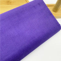 Gros plan sur le tissu velours côtelé uni 21 côtes au mètre de Longan Craft France, un tissu velours côtelé en coton doux avec de fines nervures, plié sur une surface en bois clair avec une partie d'un objet en bois à l'arrière-plan.