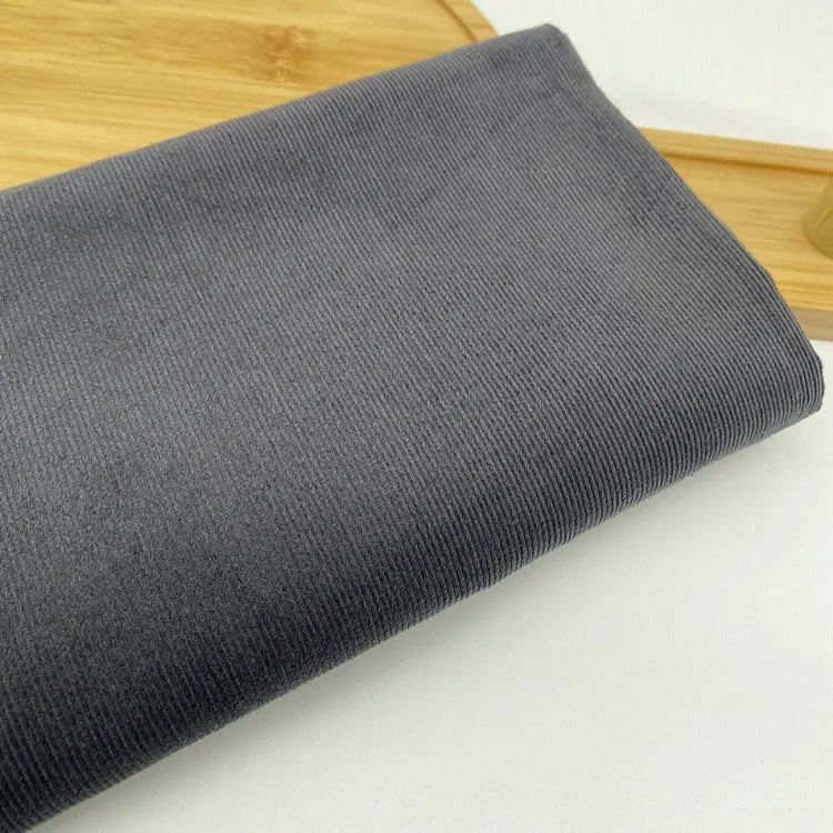 Un morceau plié de Tissu velours côtelé uni 21 côtes au mètre de Longan Craft France repose sur une surface blanche à côté d'un plateau en bois.