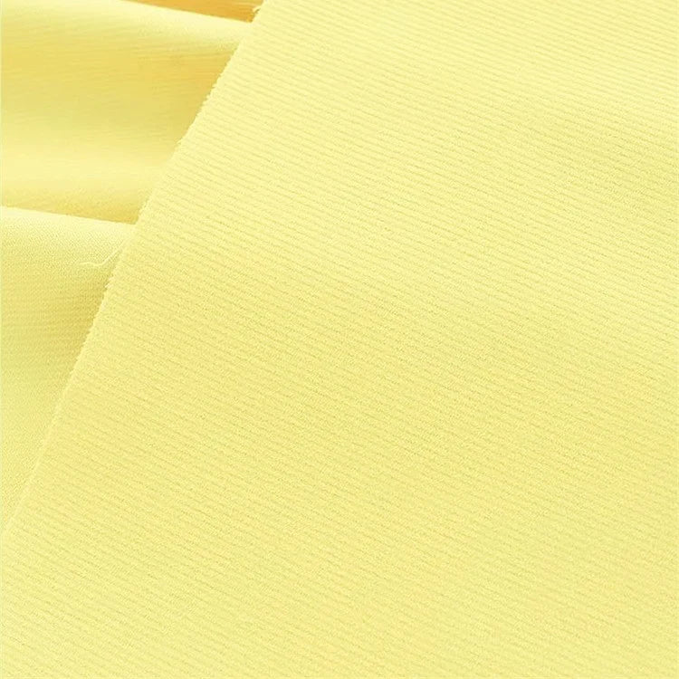 Un gros plan du tissu velours côtelé uni 21 côtes au mètre de Longan Craft France montre un coton doux, jaune clair avec de fines côtes, idéal pour les pantalons. Les délicates lignes horizontales du tissu et sa texture veloutée sont clairement visibles.