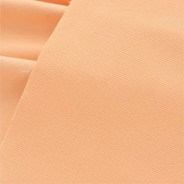 Un gros plan du Tissu velours côtelé uni 21 côtes au mètre de Longan Craft France montre sa couleur pêche claire, sa texture fine en coton côtelé et sa surface lisse. Le confortable velours côtelé est légèrement plié dans le coin supérieur gauche.