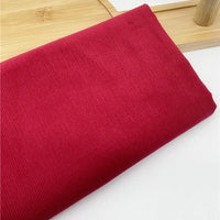 Un morceau de Tissu velours côtelé uni 21 côtes au mètre de Longan Craft France est plié sur un plateau en bois léger. Ce velours côtelé de coton, avec ses côtes fines, est parfait pour confectionner des vêtements confortables comme des pantalons.