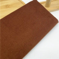 Un morceau de tissu Longan Craft France velours côtelé uni 21 côtes en coton, idéal pour vêtements, est plié sur une surface en bois clair avec un objet en bois visible à l'arrière-plan.