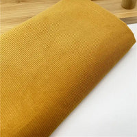 Un morceau plié de Longan Craft France Tissu velours côtelé uni 21 côtes au mètre en jaune d'or repose sur une surface blanche, montrant ses fines stries verticales - un velours de coton parfait pour créer des vêtements élégants et confortables.