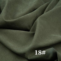 Un gros plan du microsuède polyester peau de pêche uni mi-épais au mètre de Longan Craft France montre sa texture brossée douce et veloutée en vert olive foncé, drapée librement avec des plis visibles. Le chiffre "18#" apparaît en blanc en bas à droite.