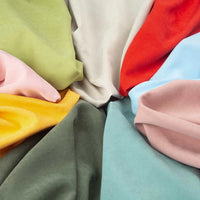 Des pièces assorties de microsuède polyester peau de pêche uni mi-épais au mètre de Longan Craft France, en vert, rose, jaune, gris, blanc, rouge, bleu et beige -tissu résistant entretien facile- sont disposées côte à côte avec des plis doux et des chevauchements.