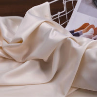 Gros plan sur le Tissu satin charmeuse uni au mètre de Longan Craft France, de couleur crème avec une surface lisse et brillante et un drapé élégant - le textile idéal pour les robes de mariée et de soirée.