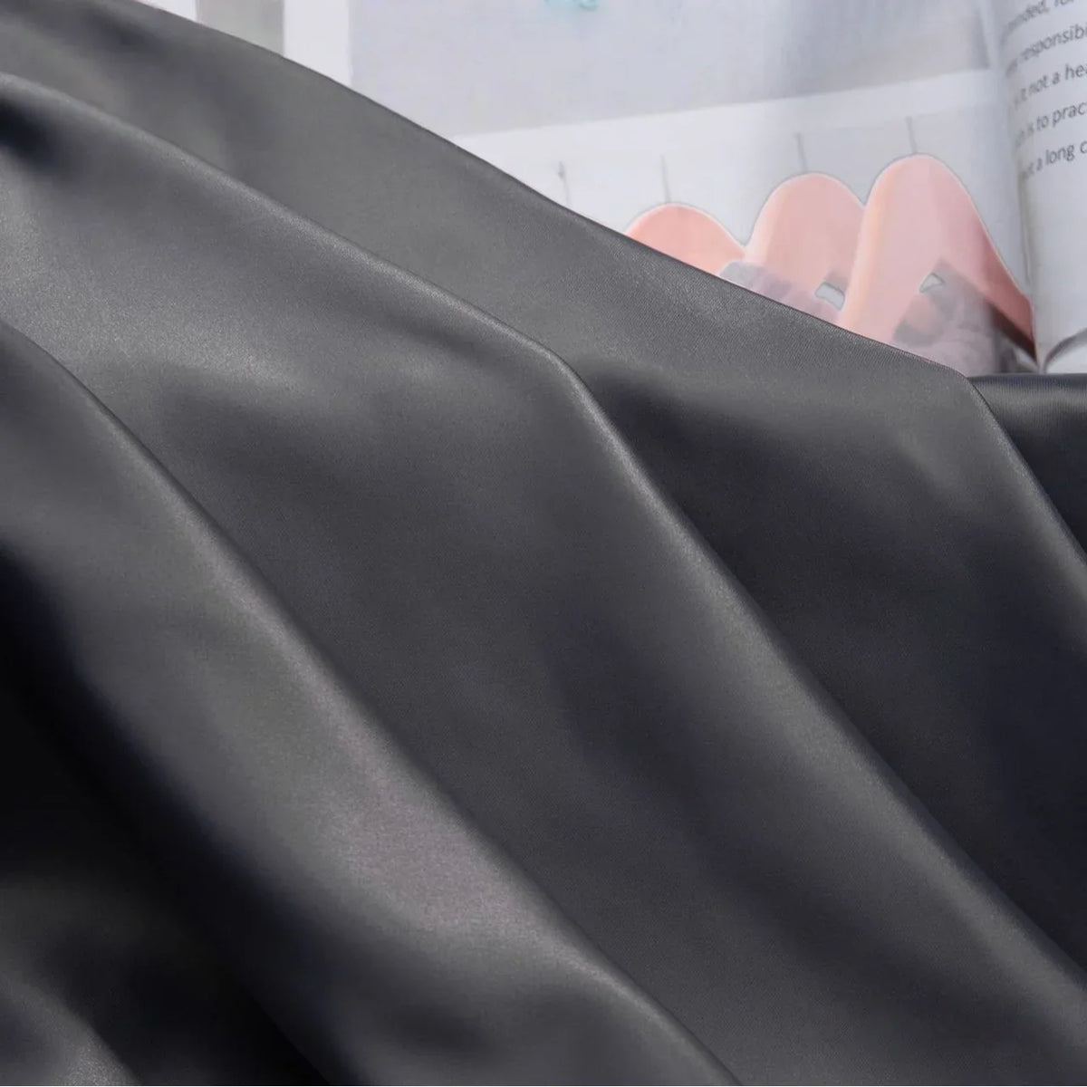 Gros plan sur la charmeuse Tissu satin uni au mètre de Longan Craft France, lisse et pliée, qui recouvre partiellement un magazine ouvert avec des diagrammes et du texte en arrière-plan - parfait pour les robes de mariée ou les robes du soir.