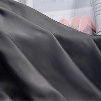 Gros plan sur la charmeuse Tissu satin uni au mètre de Longan Craft France, lisse et pliée, qui recouvre partiellement un magazine ouvert avec des diagrammes et du texte en arrière-plan - parfait pour les robes de mariée ou les robes du soir.