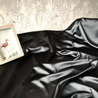 Un morceau de Tissu satin charmeuse uni au mètre de Longan Craft France est présenté sur une surface avec une illustration de flamant rose encadrée à côté, sur un mur beige texturé.