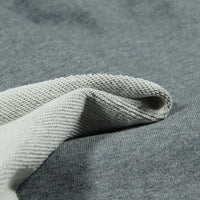 Gros plan sur le Tissu French Terry en coton uni au mètre de Longan Craft France, montrant un tissu texturé gris clair partiellement plié sur une pièce lisse gris foncé - le French Terry épais idéal pour les sweatshirts et les sweat-shirts à capuche.