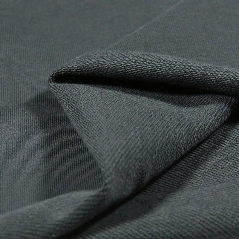 Gros plan sur l'épais Tissu French Terry en coton uni de Longan Craft France, montrant sa surface texturée gris foncé et le motif de tricot visible au verso - idéal pour les sweat-shirts à capuche.