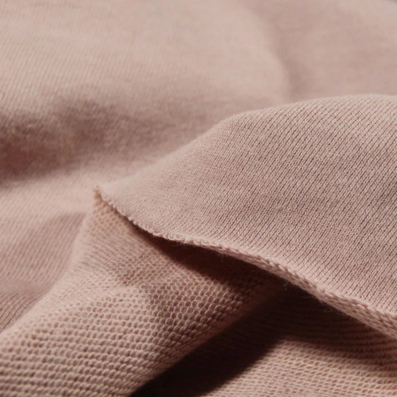 Un gros plan sur le Tissu French Terry en coton uni au mètre de Longan Craft France montre sa surface douce et texturée et ses coutures visibles. Le tissu épais est plié pour révéler les deux côtés, ce qui est idéal pour les sweat-shirts à capuche.