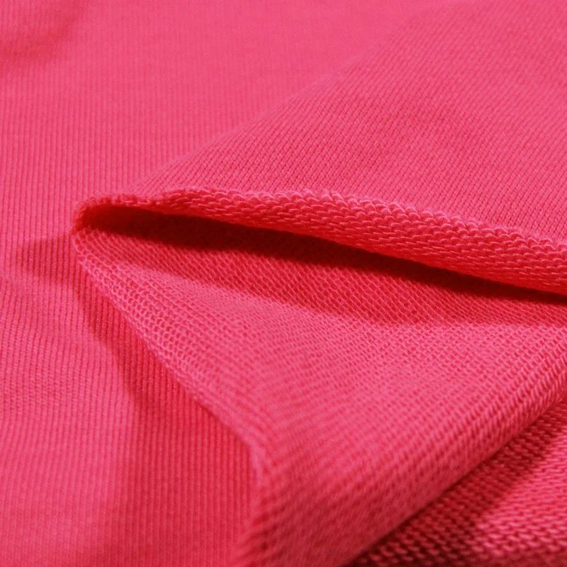 Gros plan sur le Tissu French Terry en coton uni au mètre de Longan Craft France, présenté en rose vif avec une section pliée pour montrer la texture épaisse et douce, idéale pour les sweat-shirts à capuche.